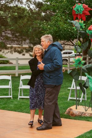 A couple dances together on a wooden dance floor surrounded by white chairs and decorative garden arrangements.