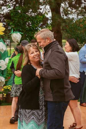 Couples dance together at an outdoor celebration on a wooden dance floor with colorful floral decorations.