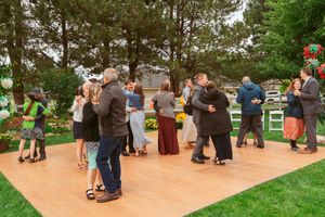 Couples dancing together on an outdoor wooden deck surrounded by green trees and grass at an outdoor event.