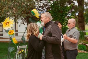 Group of people standing together in a backyard garden holding yellow balloons and flowers during an outdoor gathering.