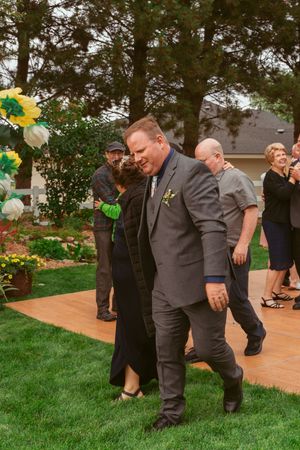 Guests enjoy an outdoor wedding reception on a wooden dance floor decorated with yellow and green balloons.
