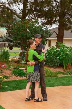 Couple dancing together on an outdoor patio surrounded by landscaped garden and trees.
