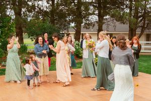 Wedding guests in pastel dresses gathering on a wooden dance floor in an outdoor garden setting.