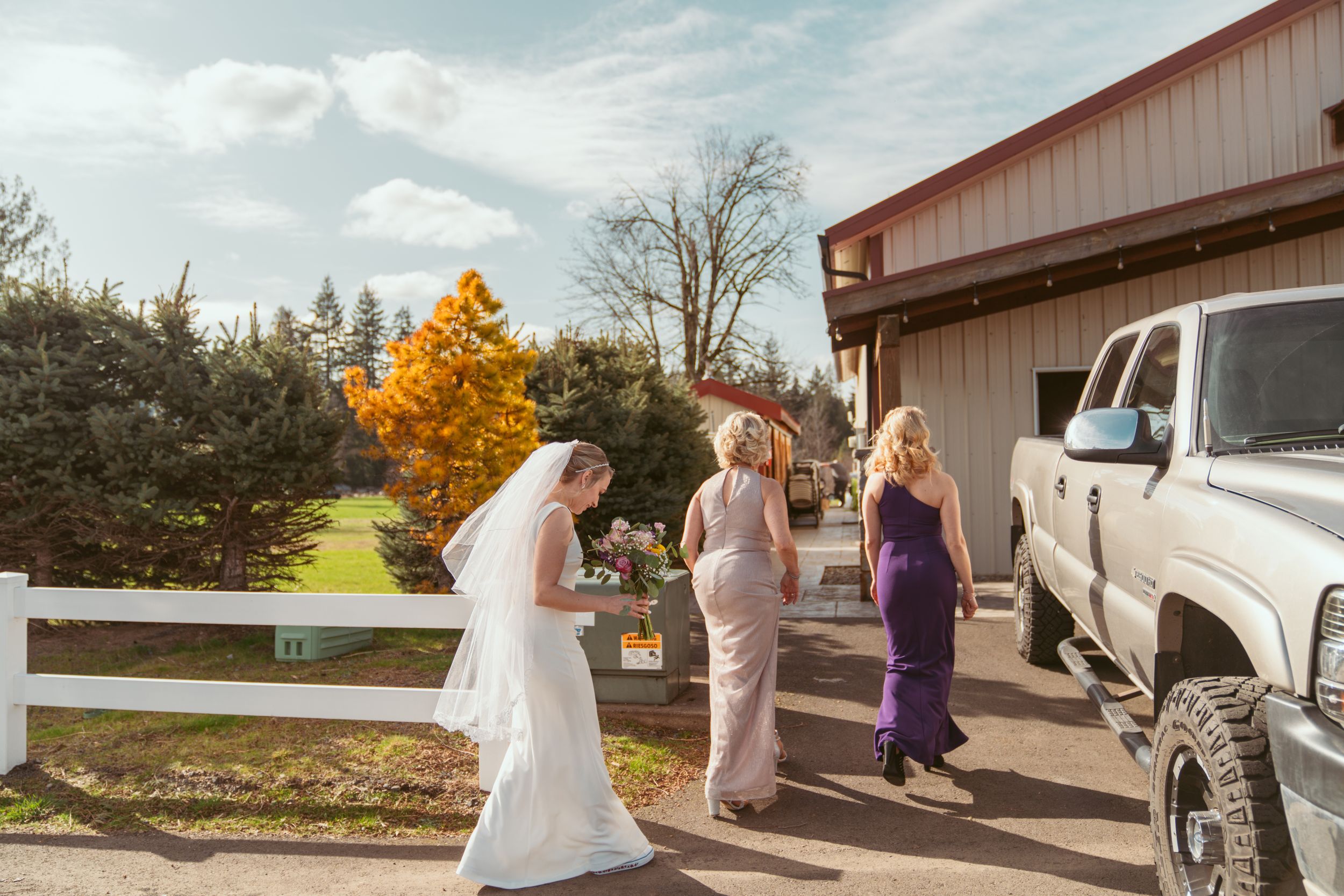 Wedding party walking near a rustic barn with a truck parked outside on an autumn day with golden foliage.