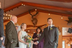 Wedding party members line up in front of a rustic wood-paneled wall with warm lighting and mounted deer antlers.