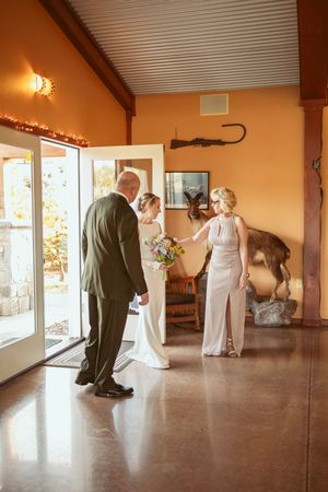 A warm-toned wedding venue interior with guests gathered near glass doors decorated with string lights.