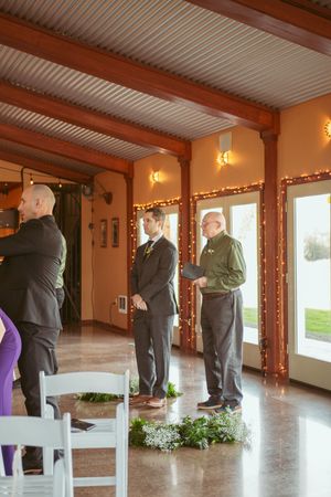Wedding ceremony setup in an elegant room with wood beams and string lights along orange-tinted walls.