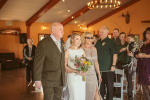 Wedding party walking down the aisle at a rustic indoor venue with wooden beams and chandelier lighting.
