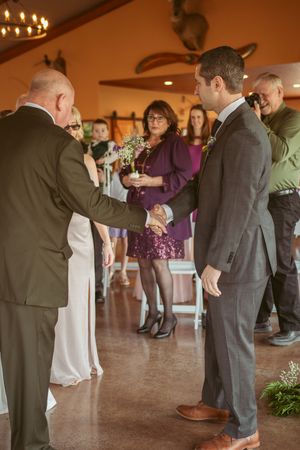 Wedding guests mingling in formal attire inside a rustic venue with decorative lighting.