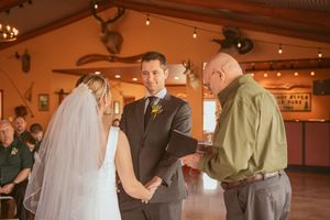 A couple exchanging wedding vows during an indoor ceremony with warm lighting and guests in attendance.
