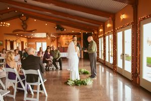 Wedding ceremony taking place in a rustic venue with wooden beams and large windows overlooking a scenic view.
