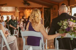 Wedding attendees seated in white chairs during indoor ceremony with decorative lighting.