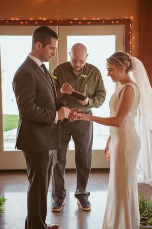 Wedding ceremony exchange of rings during intimate indoor ceremony with natural lighting.