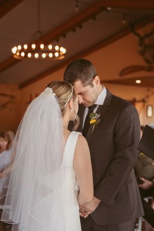 An intimate wedding moment under a circular chandelier in a rustic indoor venue.