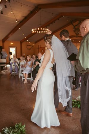 Wedding ceremony in a rustic venue with string lights and guests seated in the background.