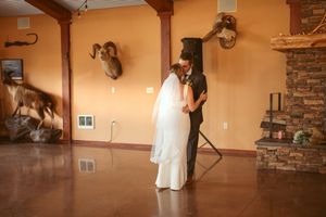 Wedding couple embracing in rustic venue with mounted decor and stone fireplace.