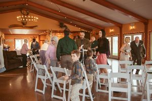 Wedding guests mingle and stand around white folding chairs in an elegant reception hall with chandeliers.
