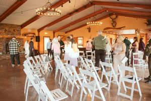 A wedding venue decorated with string lights features rows of white folding chairs and exposed wooden beams.