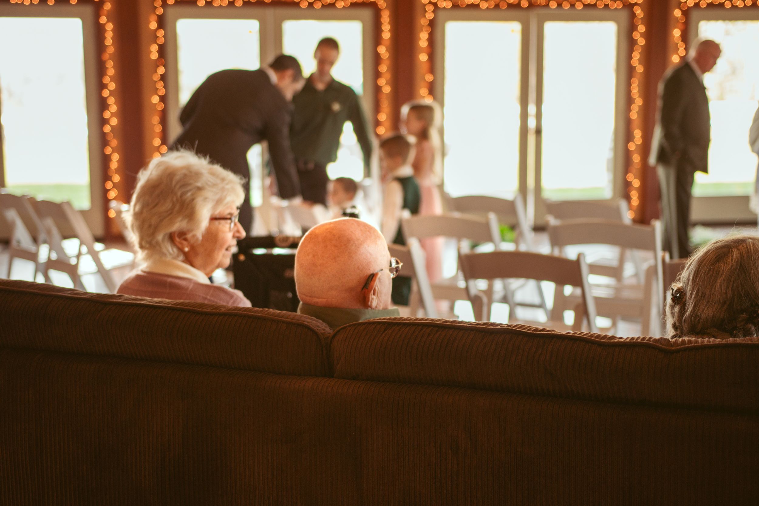 Guests seated at a wedding ceremony venue decorated with twinkle lights and wooden accents.