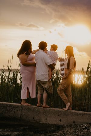 Family group stands together watching golden sunset through tall reeds.