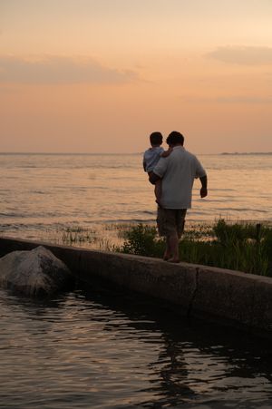 Silhouettes sit together watching sunset over calm waters near a rocky shore, Connecticut photography.
