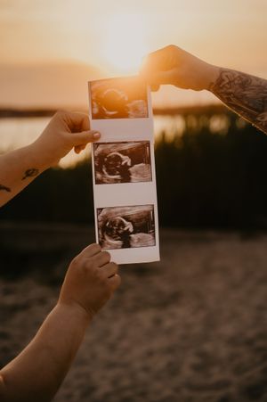 Hands hold ultrasound photos against dramatic sunset sky backdrop.