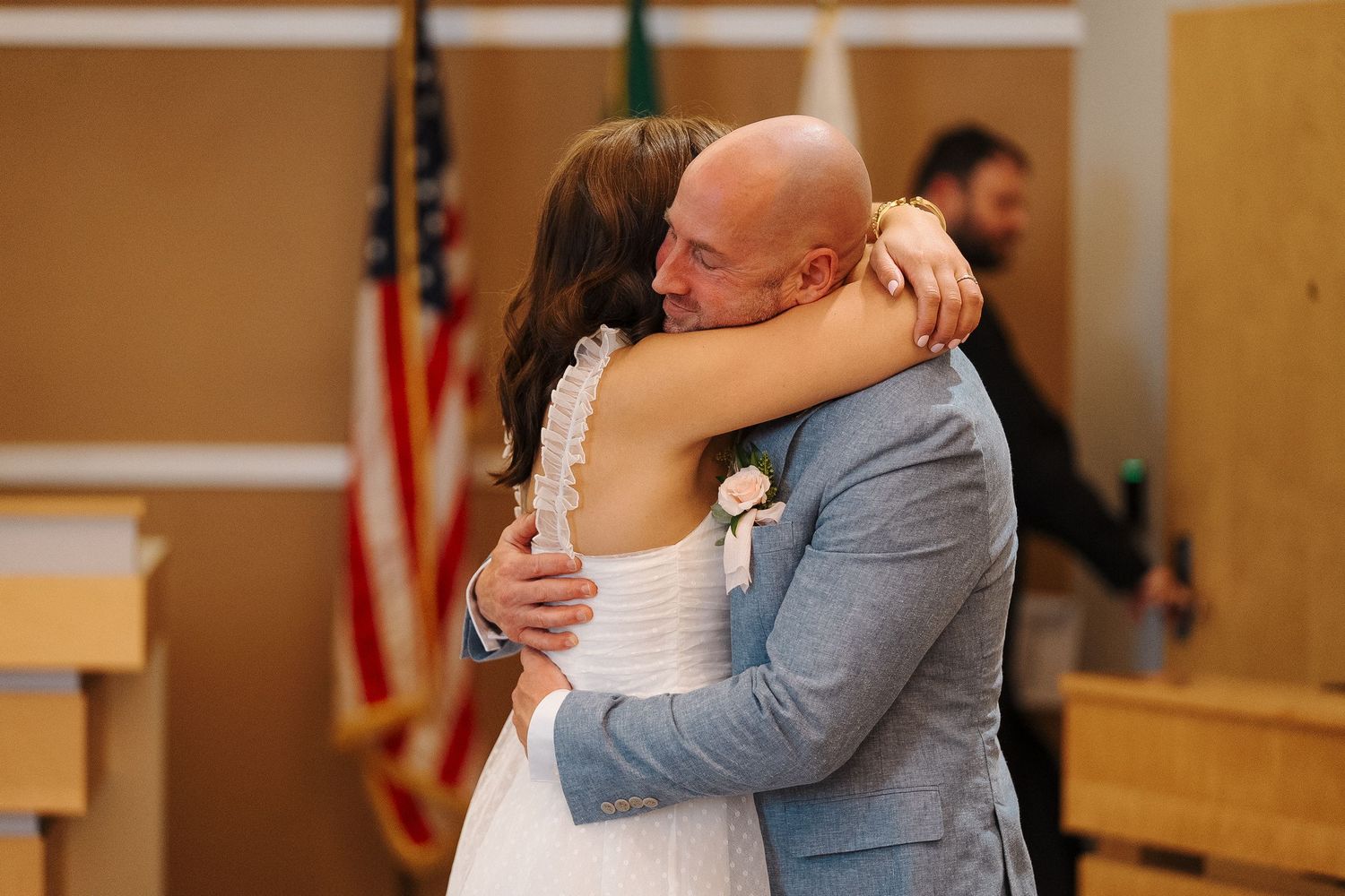 Newly married couple embrace in an emotional hug after their wedding ceremony while standing before an American flag.