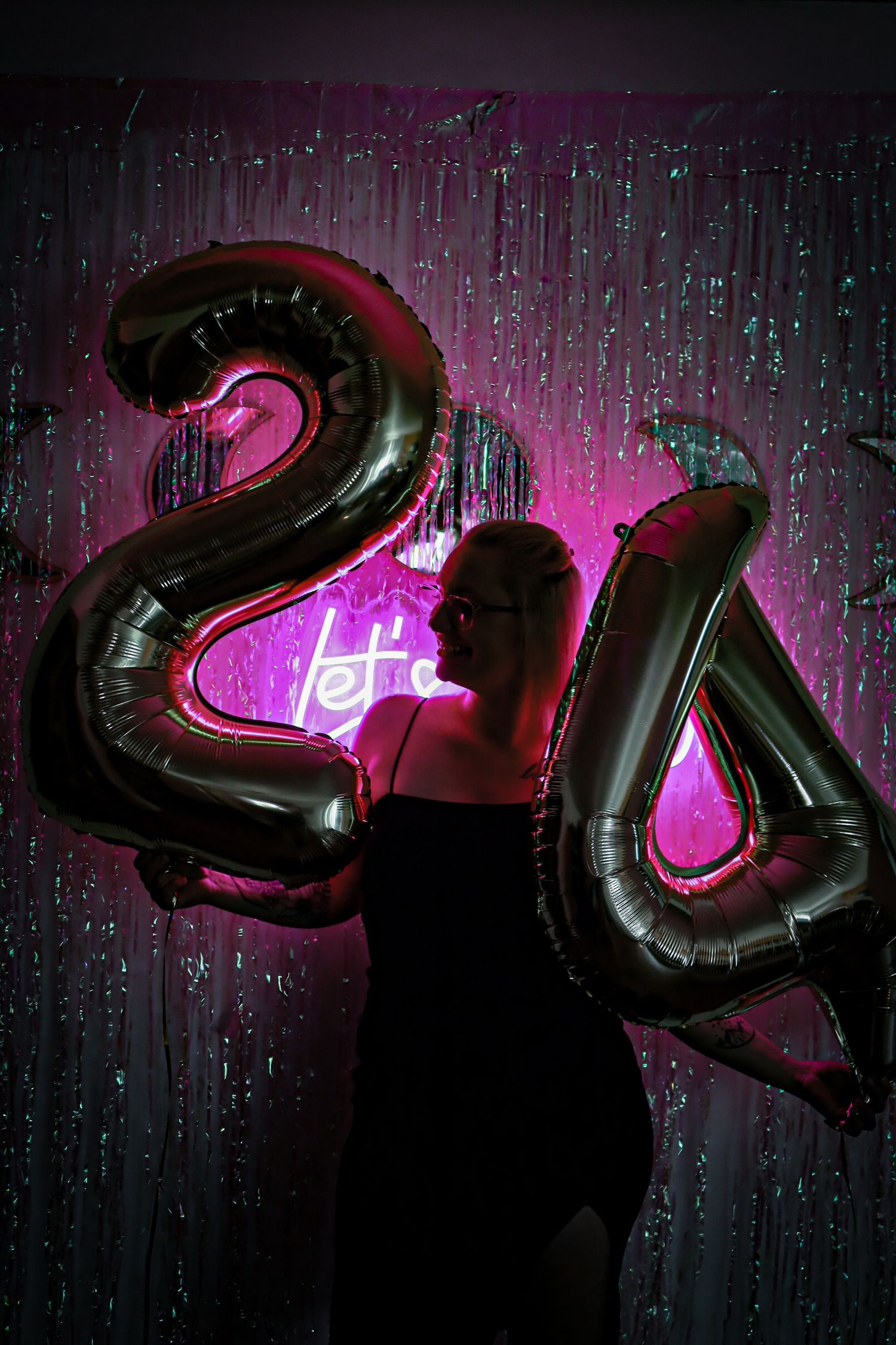 Black metallic balloon numbers against dark background with neon pink lighting glowing through rain or water droplets.