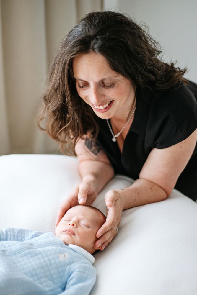 Mother in black shirt lovingly gazes at sleeping baby while giving gentle head massage.