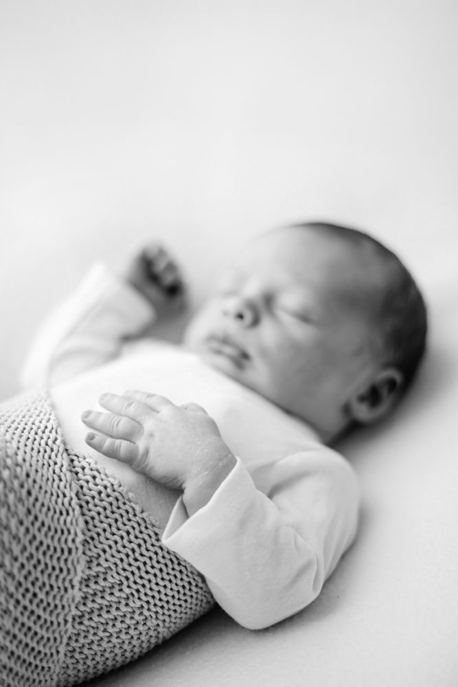 A series of black and white photos showing a sleeping baby swaddled in a knit blanket with soft lighting and minimal contrast.