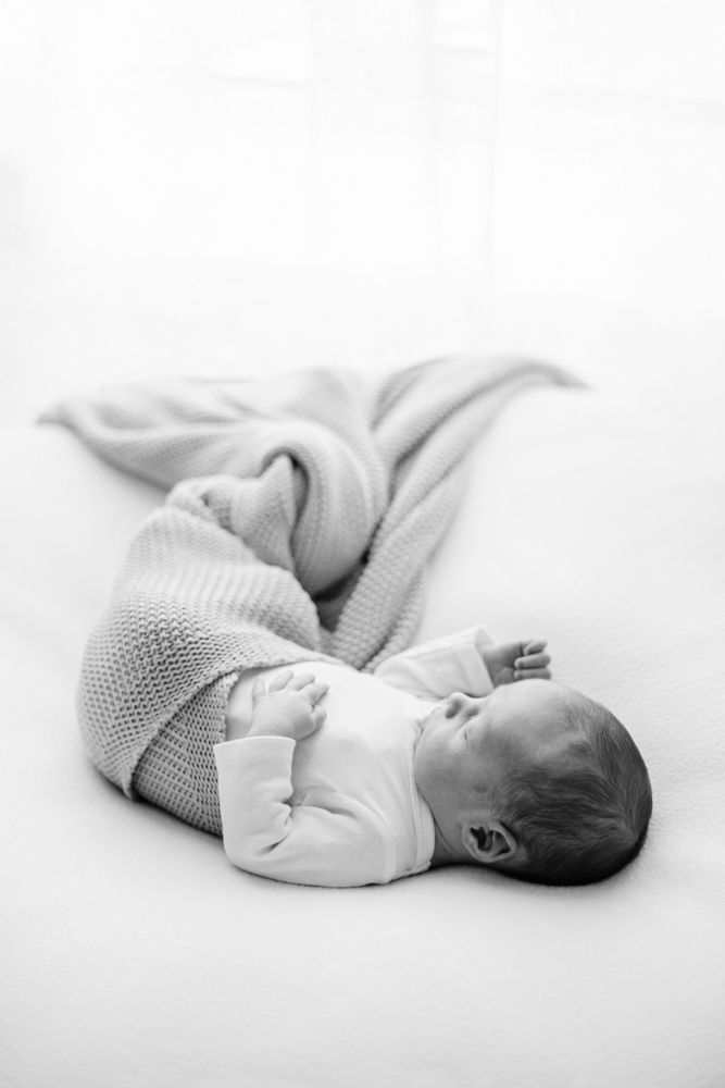 Black and white photo of sleeping newborn baby wearing knit sweater on white background.