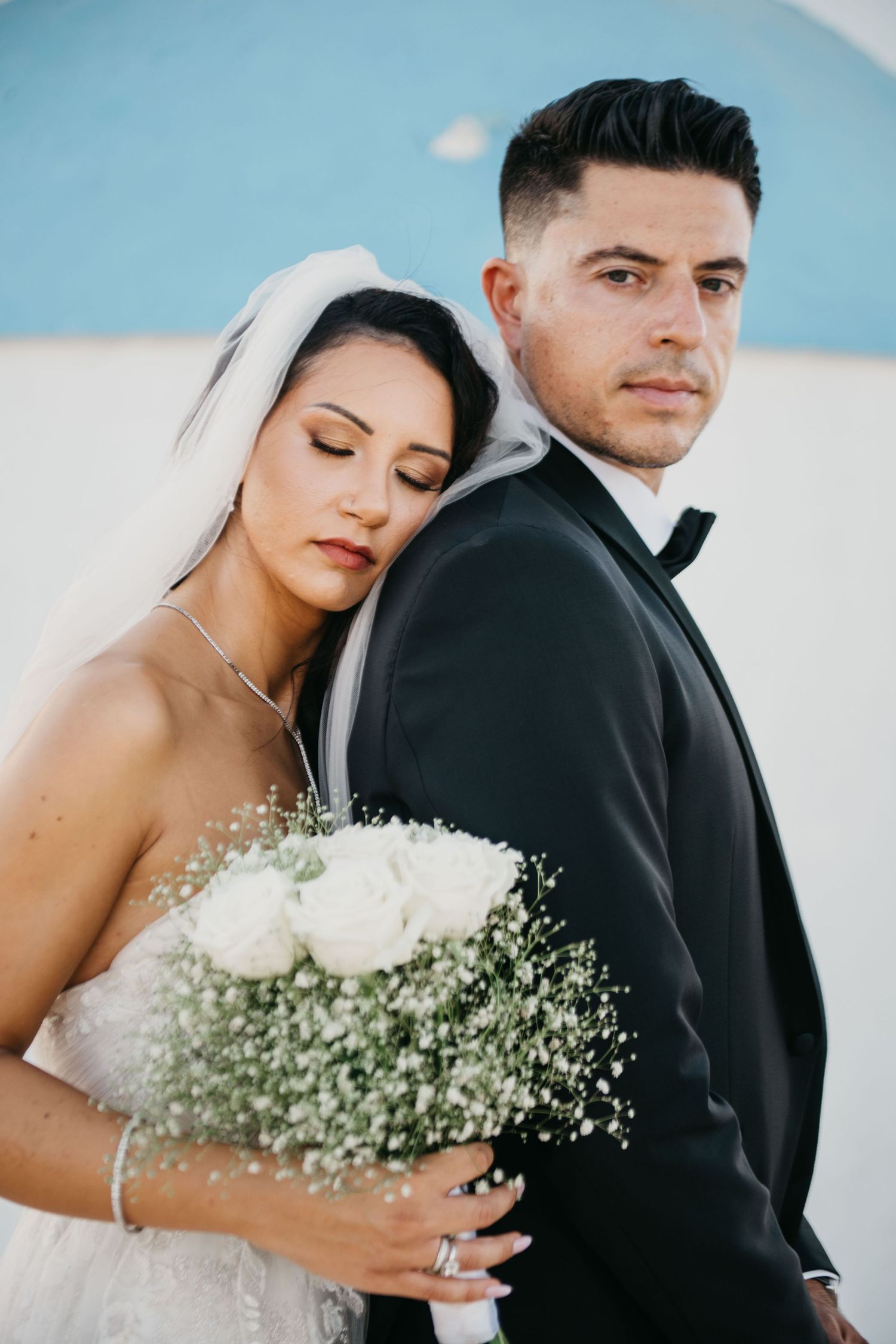 A newlywed couple walks together on a sandy path as the bride's white dress flows elegantly in the breeze.