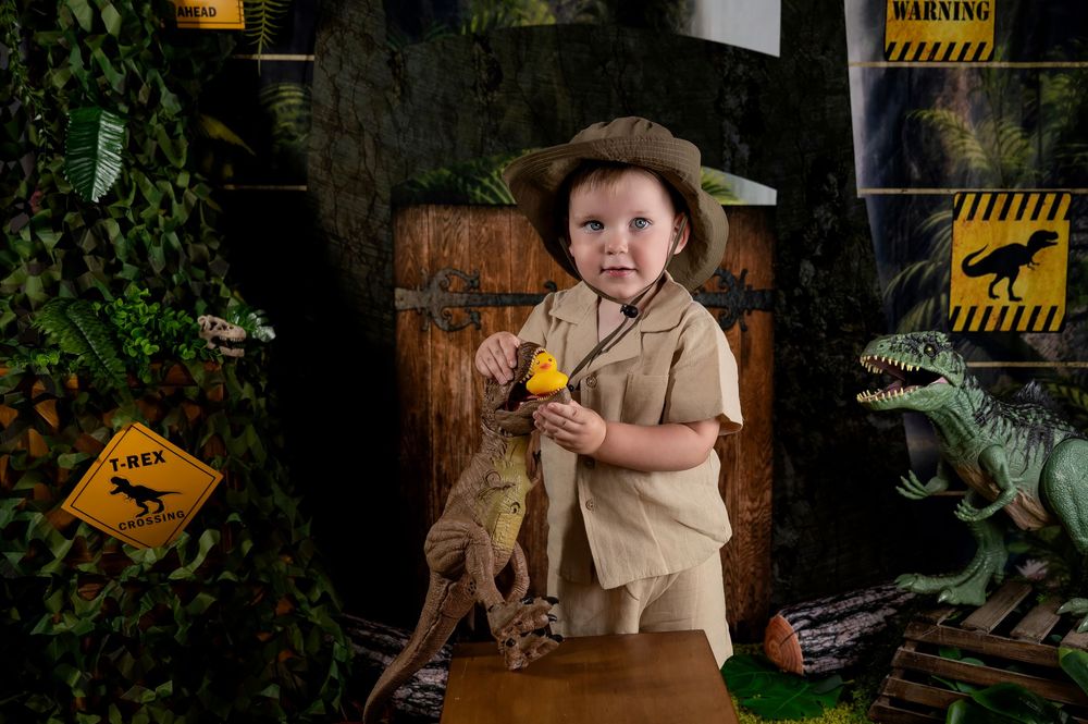 Safari-themed photo setup with a wooden backdrop and dinosaur decorations featuring explorer-themed clothing and props.