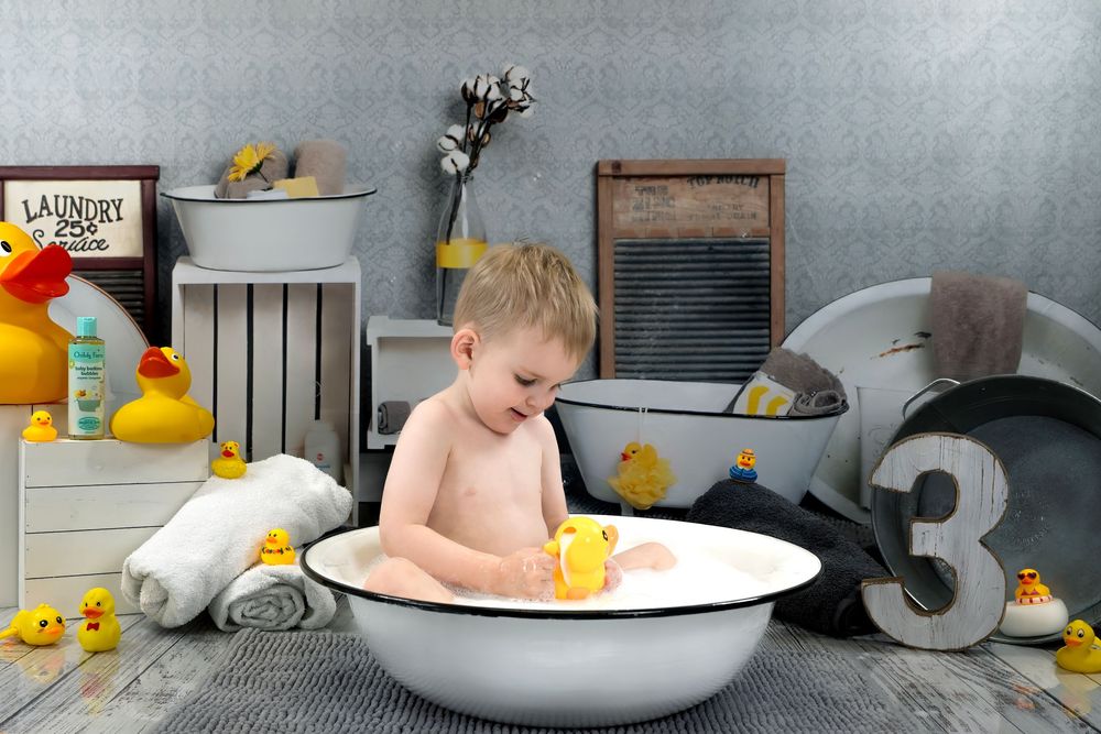 A child in a metal washtub surrounded by rubber ducks with vintage decor and oversized number 3 in the background.