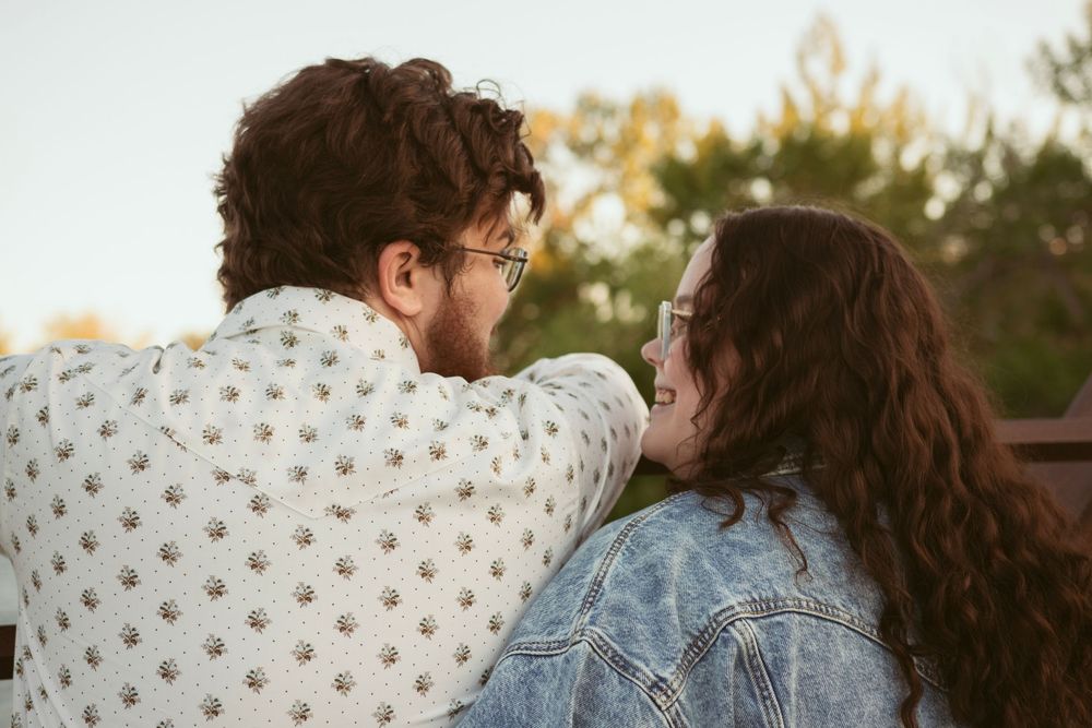 Two people in casual attire sharing a tender moment outdoors during golden hour while looking away from camera.