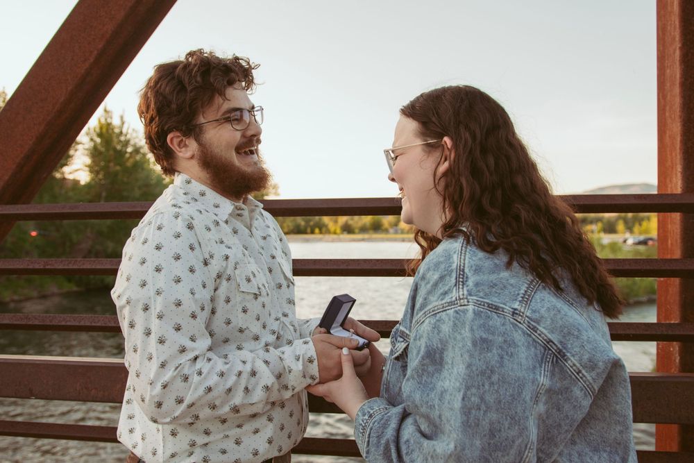 Two people laughing together on a bridge during sunset while looking at their phones.