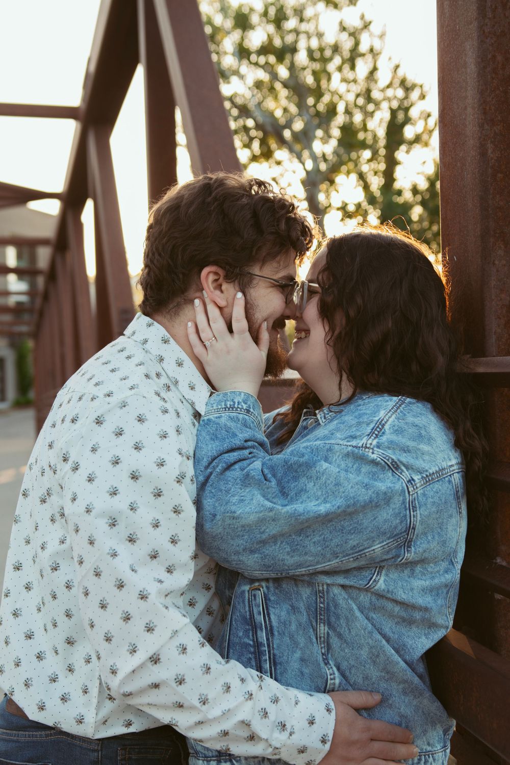 Intimate couple sharing a tender moment on a rustic bridge at sunset wearing denim and casual attire.