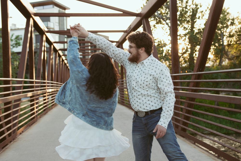Couple dancing playfully together on a metal bridge during golden hour sunset.