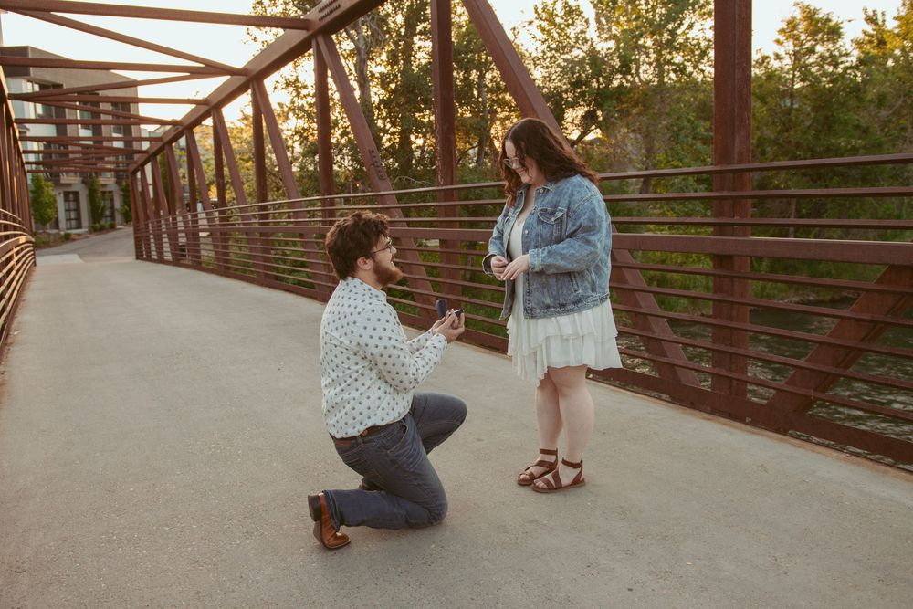 Two people share a special moment during sunset on a rustic metal bridge with railing.