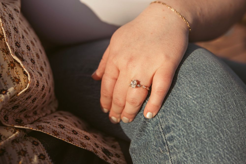 Close-up view of a person's hand wearing a gold ring with a small center stone and resting on denim material.