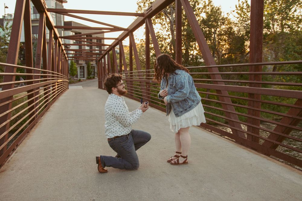 Two people share a special moment on a rustic metal bridge at sunset with golden light filtering through the trees.