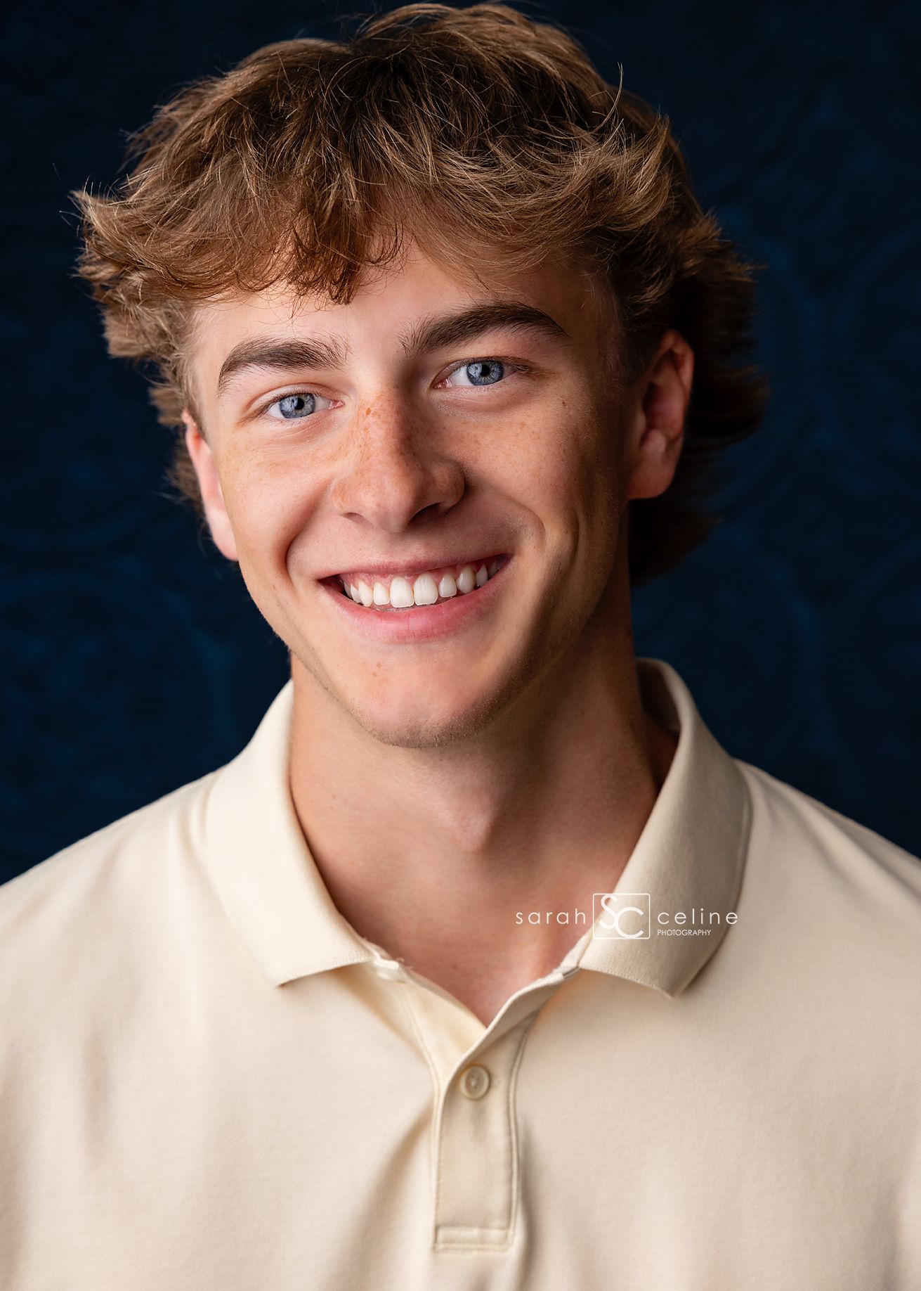 Professional portrait of someone wearing beige polo shirt against dark blue background, smiling warmly.