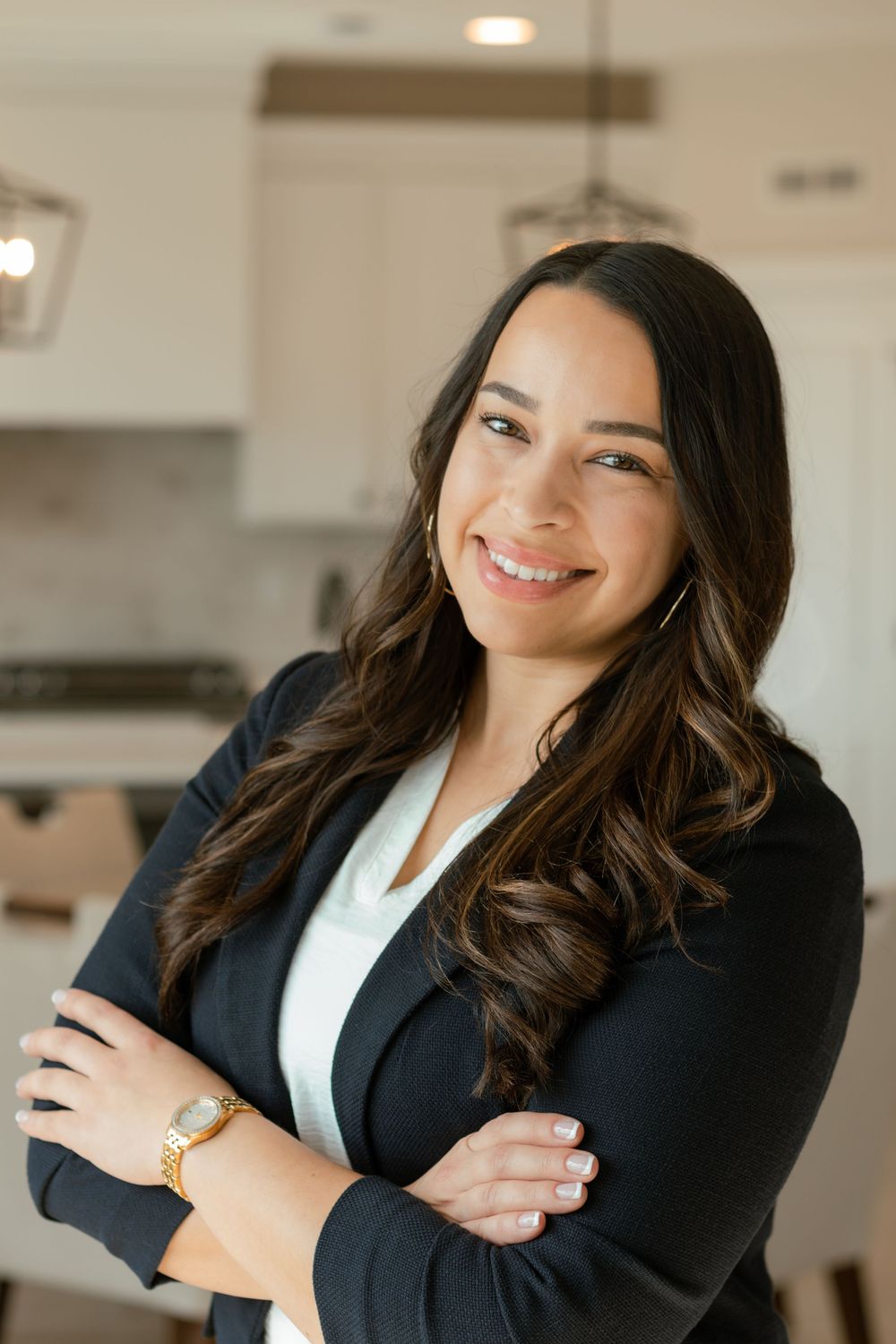Branding headshot of female realtor in navy blazer with arms crossed, smiling confidently in bright kitchen setting