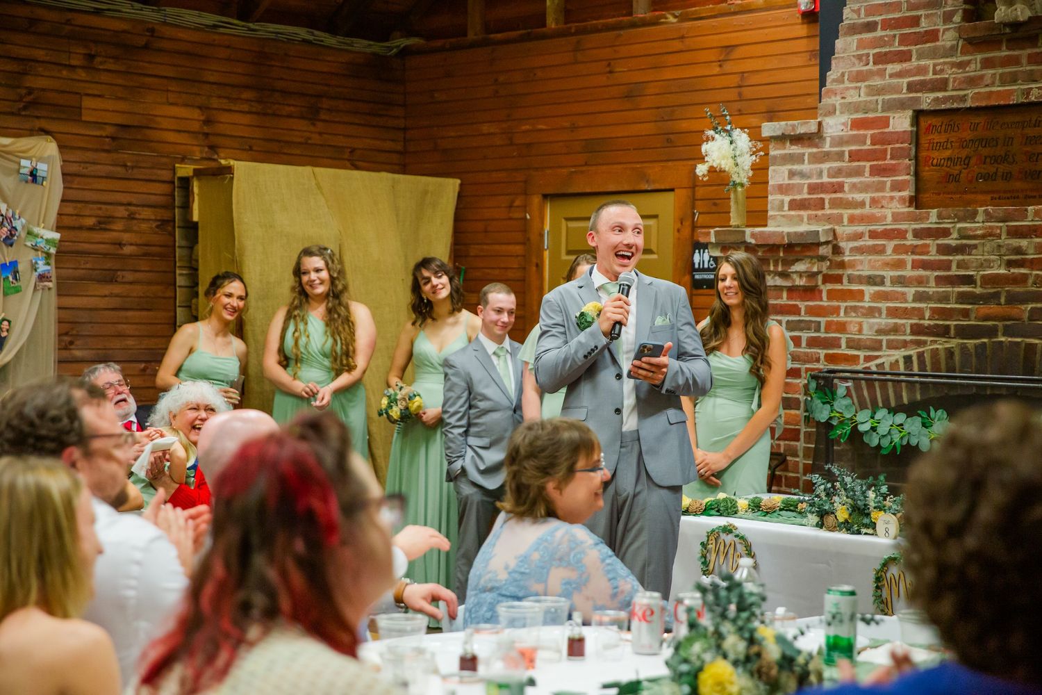 A lively moment during a wedding reception in a rustic brick and wood venue with people celebrating around dining tables.