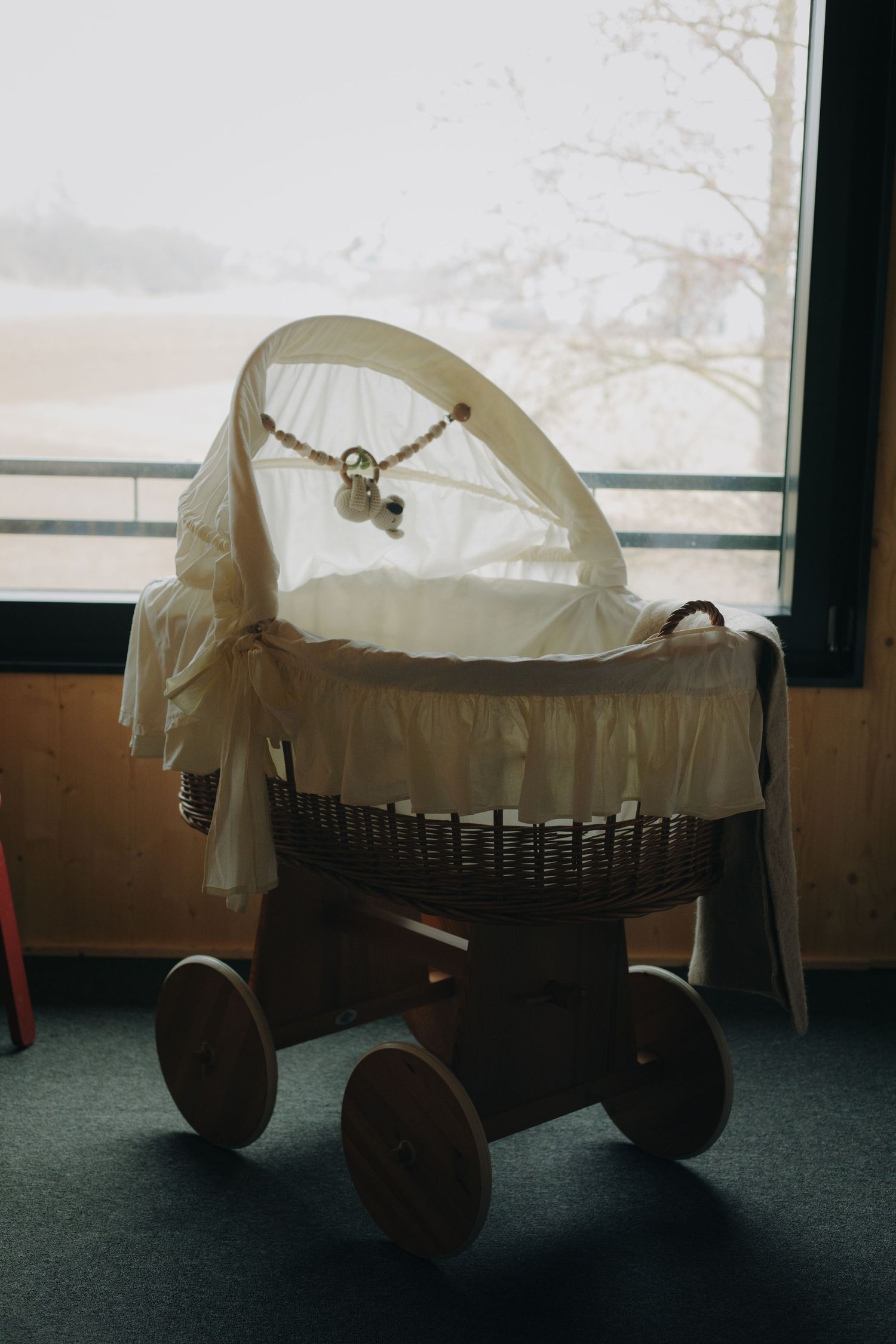 Vintage-style baby carriage with white canopy by window in moody lighting.