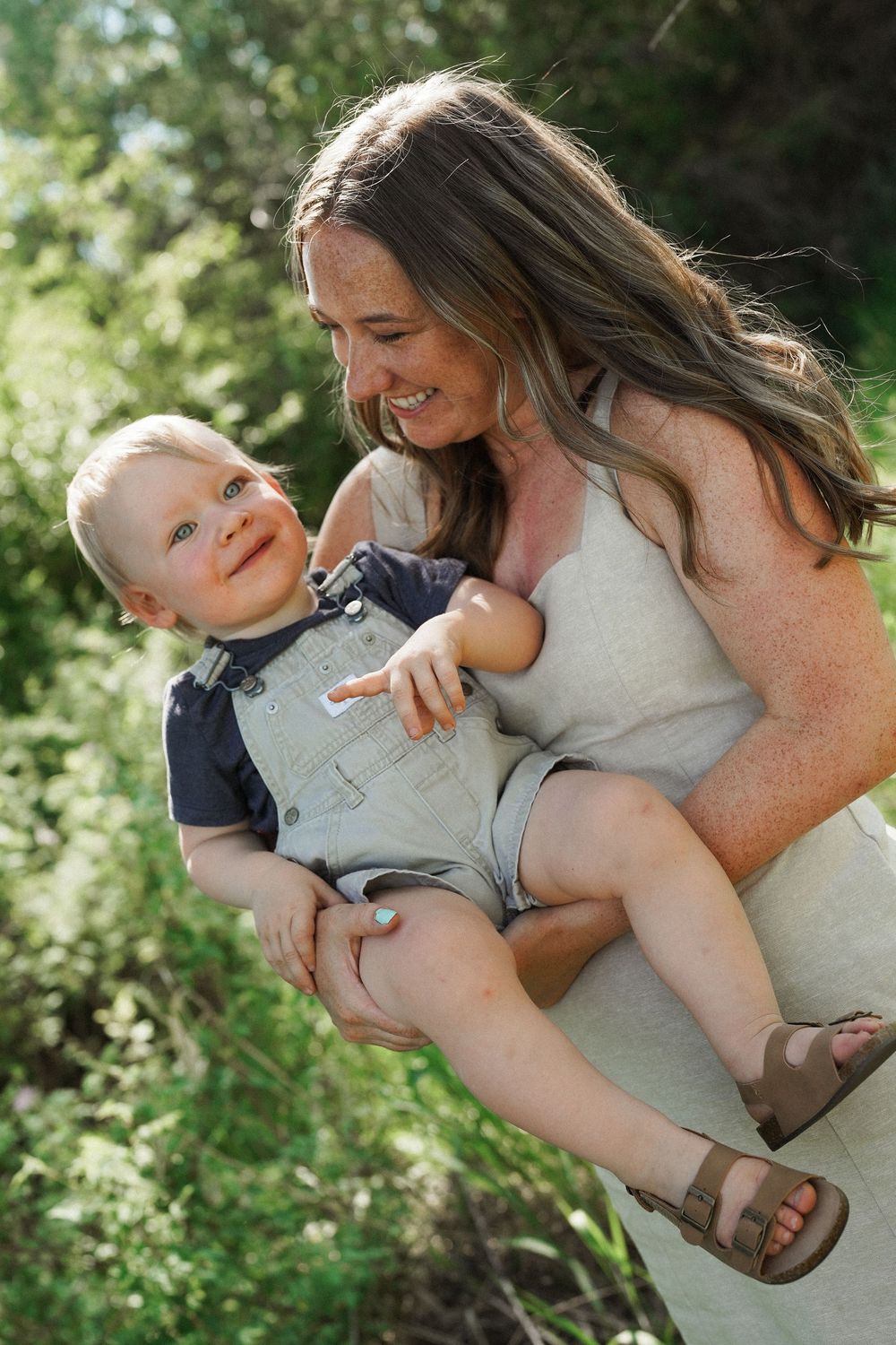 Parent and child share a playful embrace outdoors during a sunny photoshoot in nature.