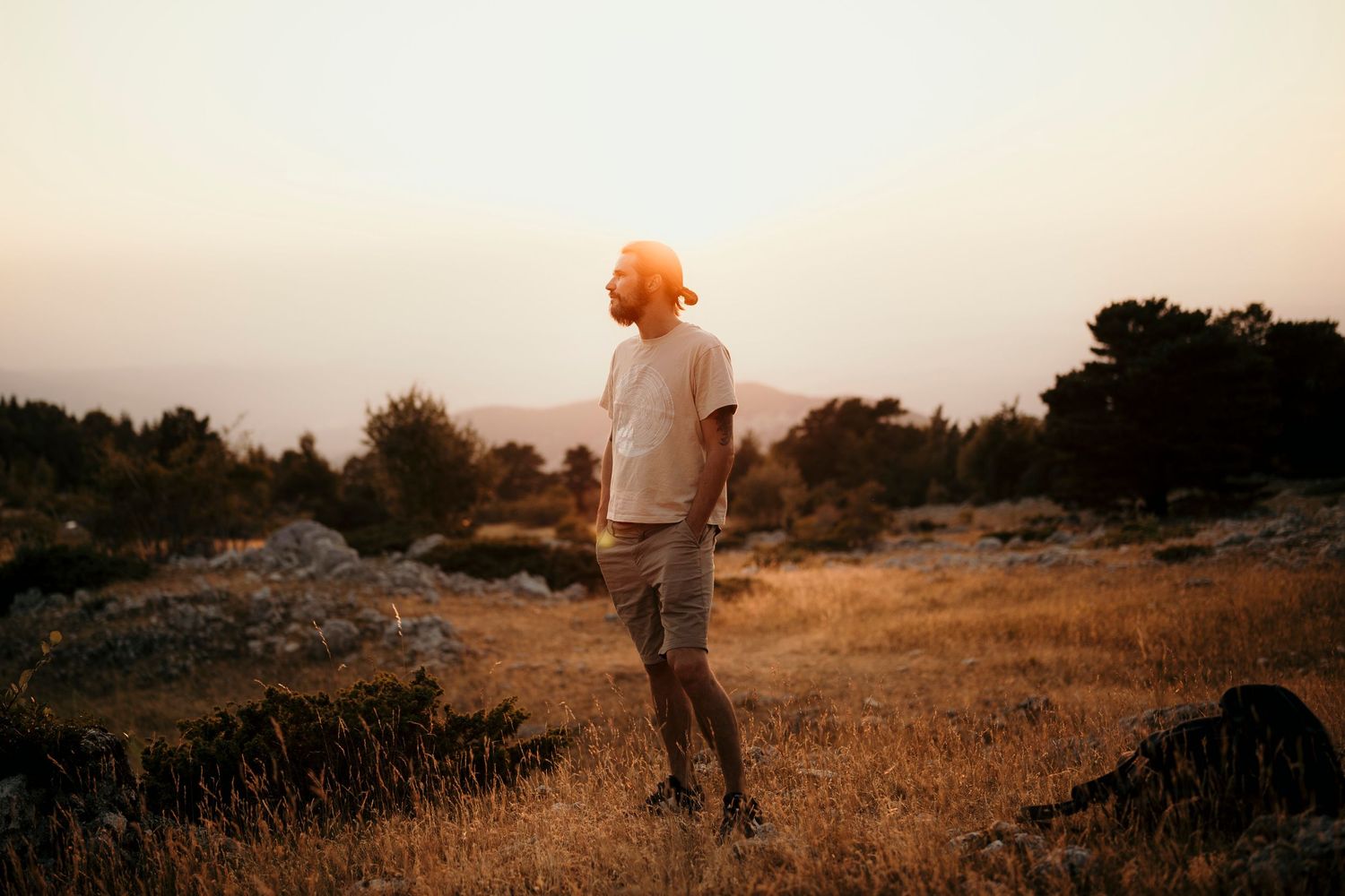 A person in casual attire stands alone in a golden field during sunset.