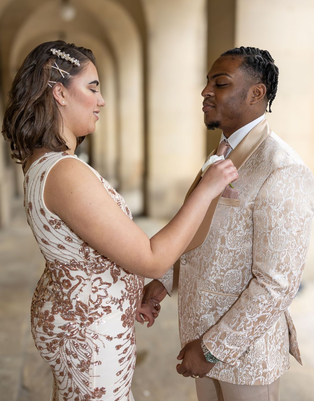 A couple in formal attire shares an intimate moment during their wedding photoshoot in an elegant hallway.