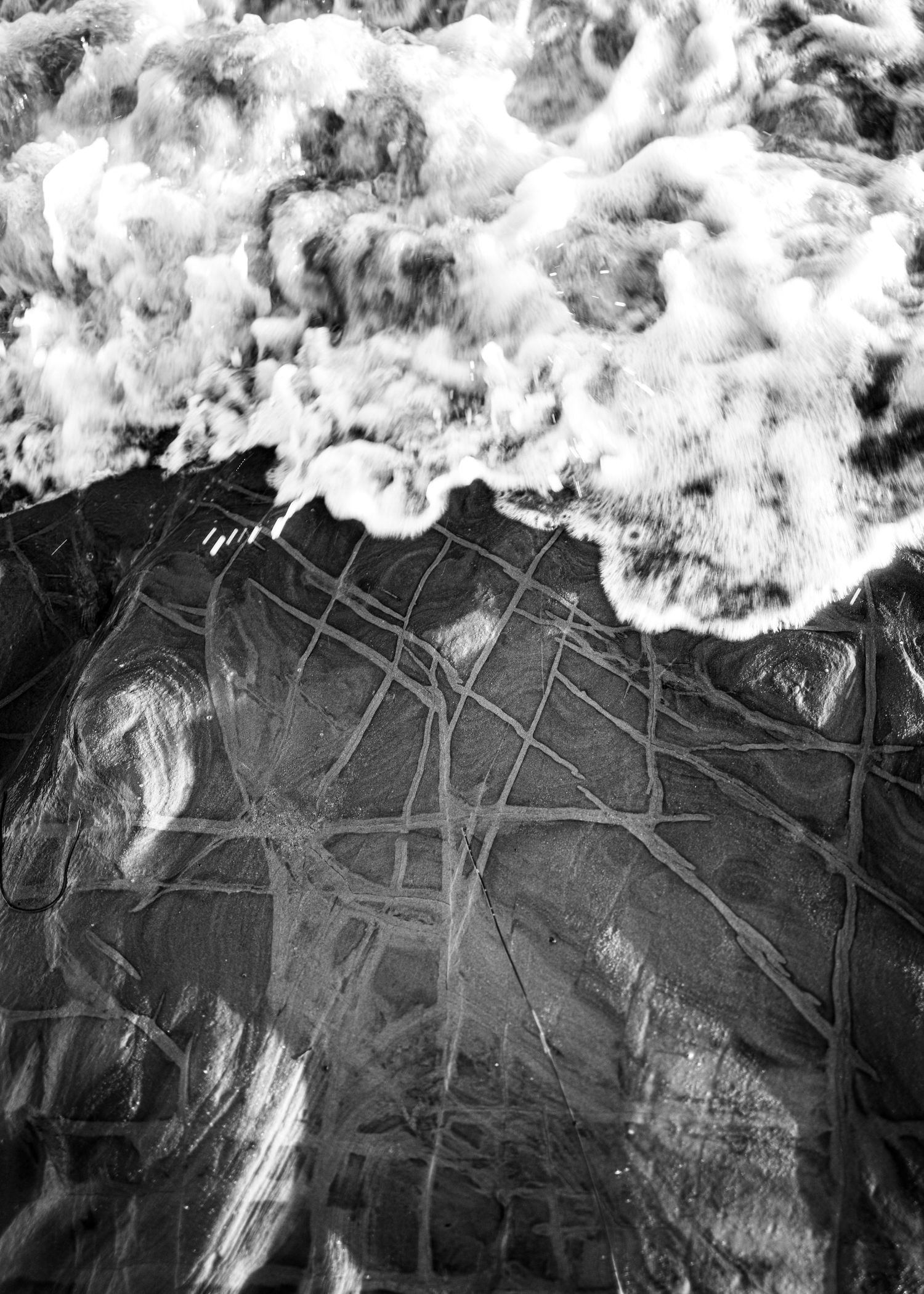 Black and white aerial view of ocean waves crashing over a textured rock surface.