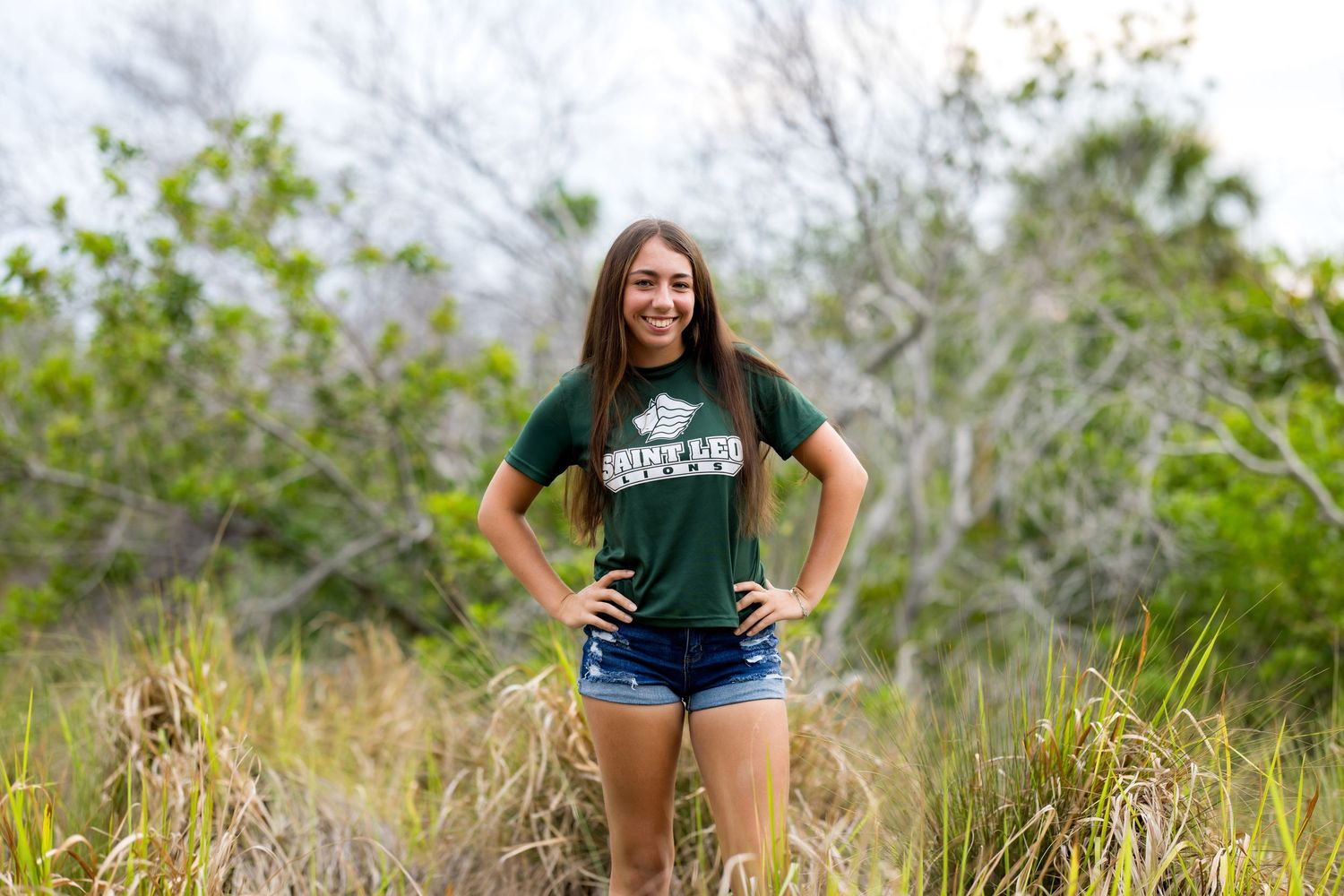Woman in green shirt and denim shorts standing in natural grass field setting.